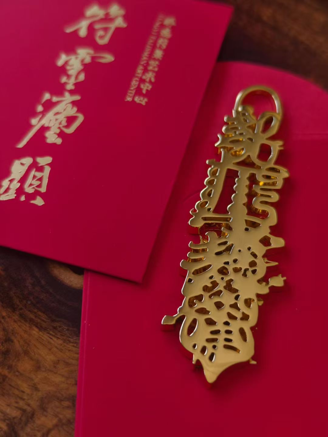 Gold laser-cut Caishen metal blessing charm on a red envelope